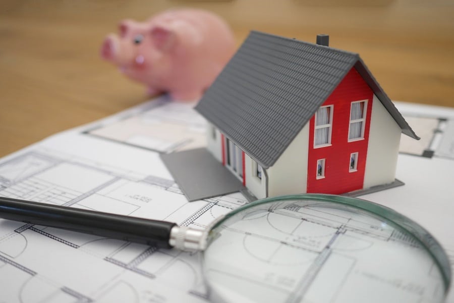 Small model house between magnifying lens and piggy bank