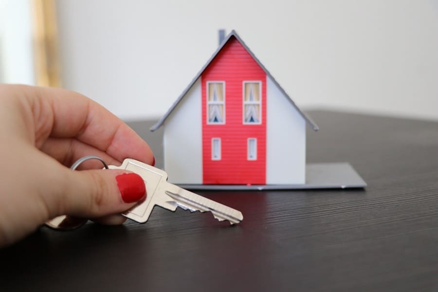 Hand holding a house key and a tiny house model on a table