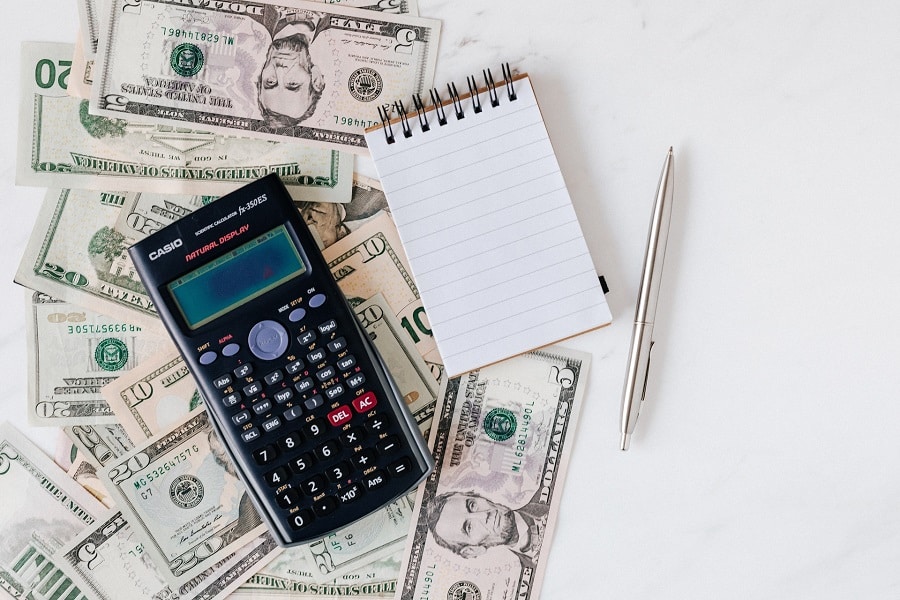 A calculator and notepad placed on top of dollar bills