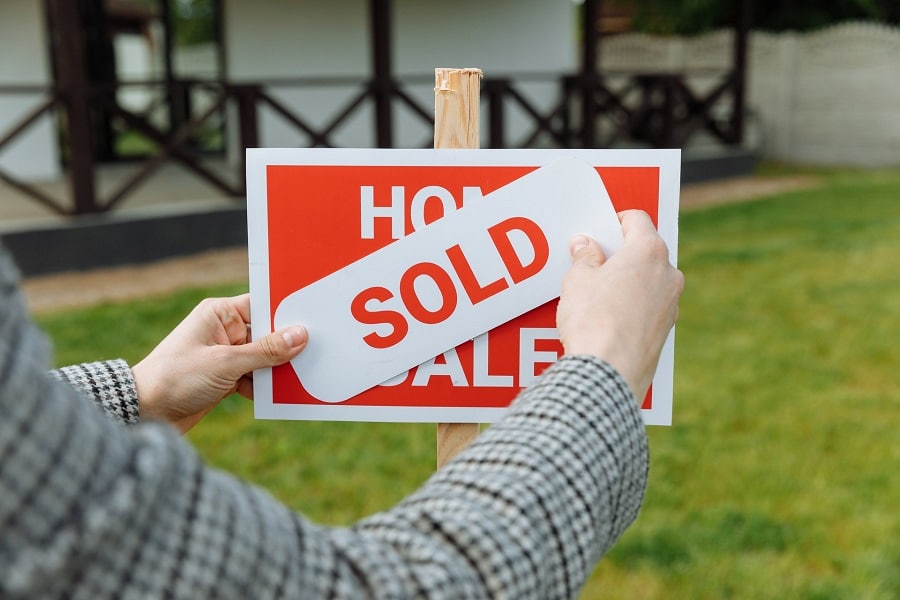 Person putting a sold sticker on a sign