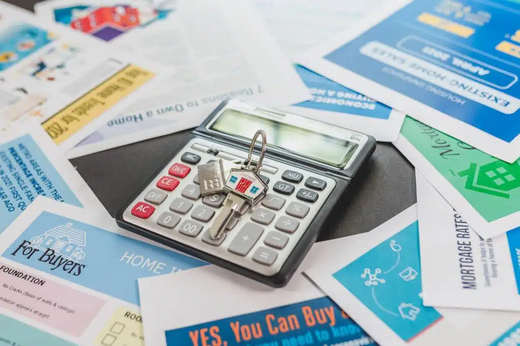 A house key placed on a calculator and surrounded by real estate brochures